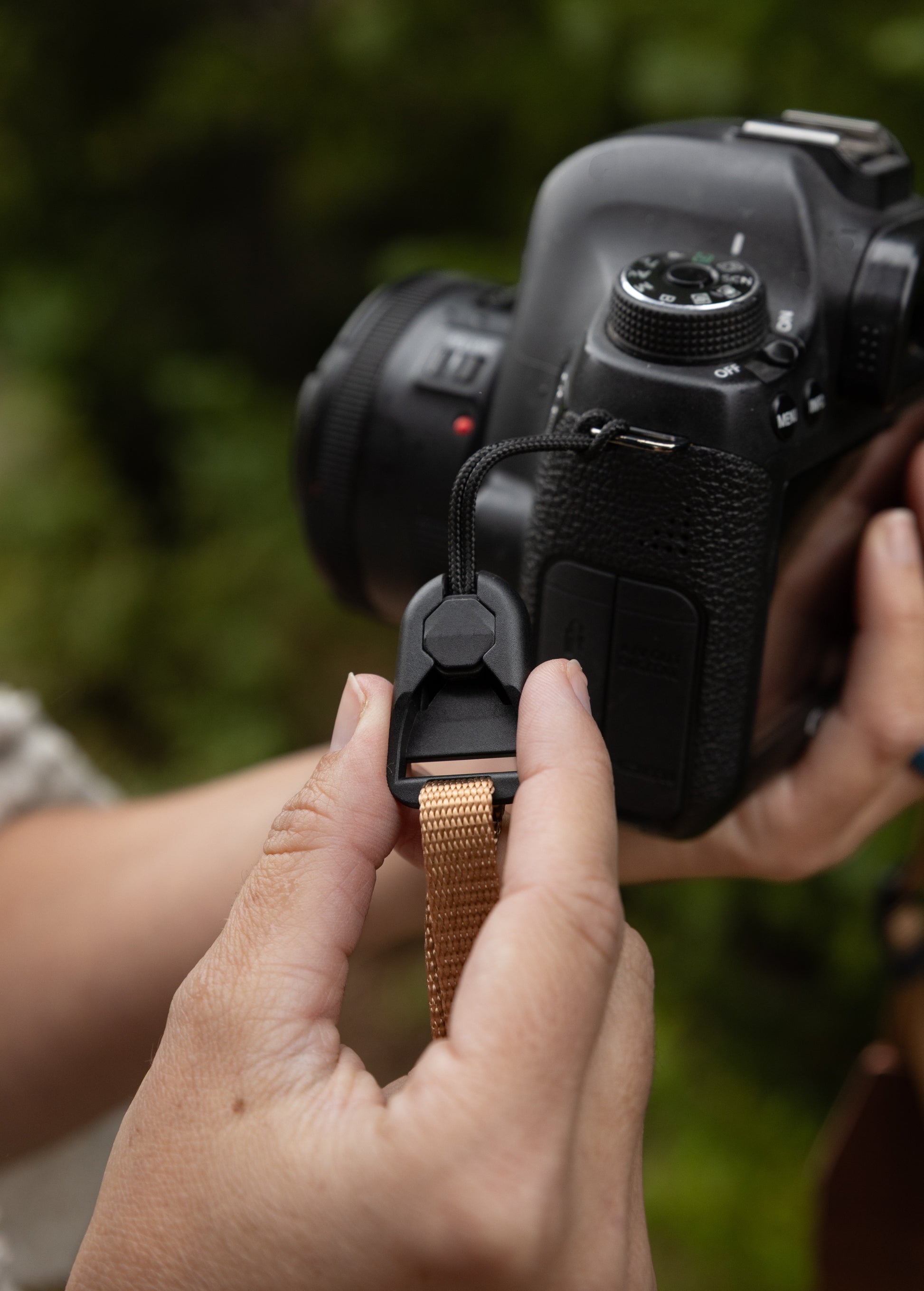 Close-up of hands attaching a tan camera strap to a low-profile quick-release buckle connector secured to the camera body