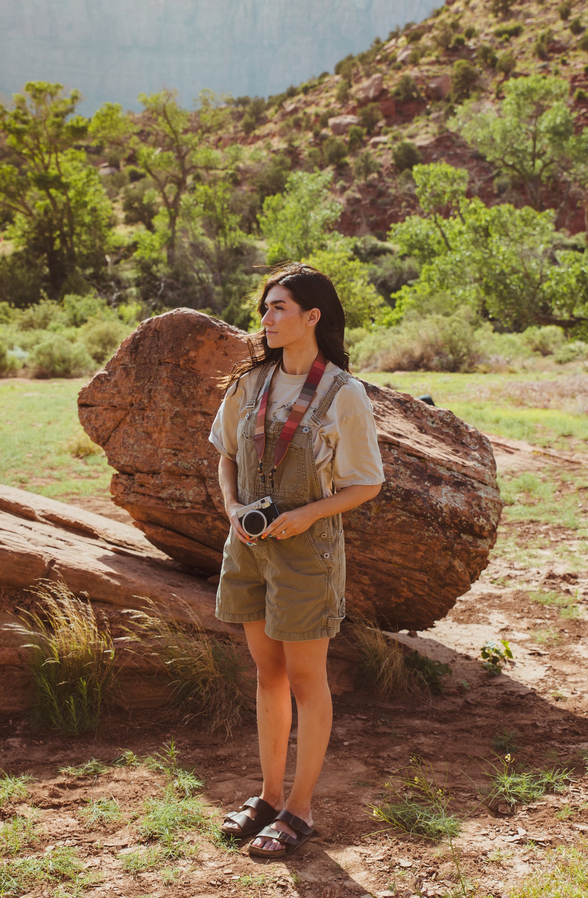 women in field standing with Retro striped camera strap hanging from women's neck holding film camera