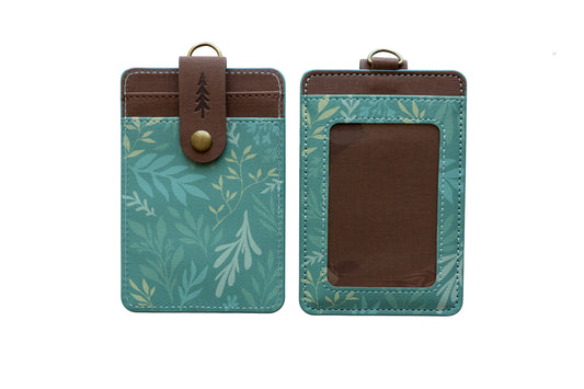 A studio product shot showing both the front and back of the green botanical ID holder isolated on a white background. It provides a clean, clear view of the clear ID window, back card slots, and pine tree snap closure.