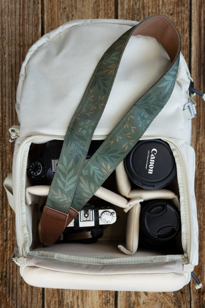 Top-down view of the "Silent Grove" camera strap coiled inside a camera bag, showcasing the green floral pattern and brown backing.