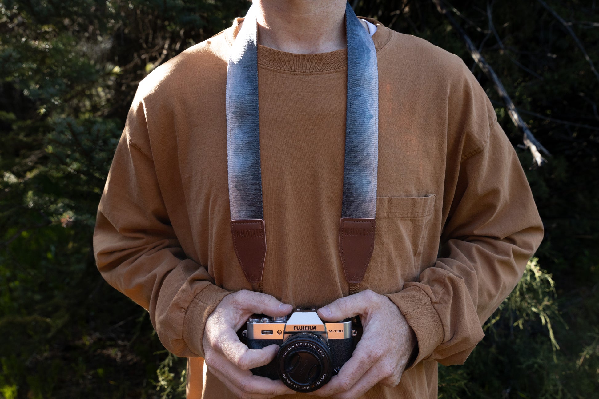 Silent Summit camera strap front view highlighting how the blue-to-gray nature-inspired patterned strap hangs around the neck with distinct brown leather endpoints connected to a camera body.