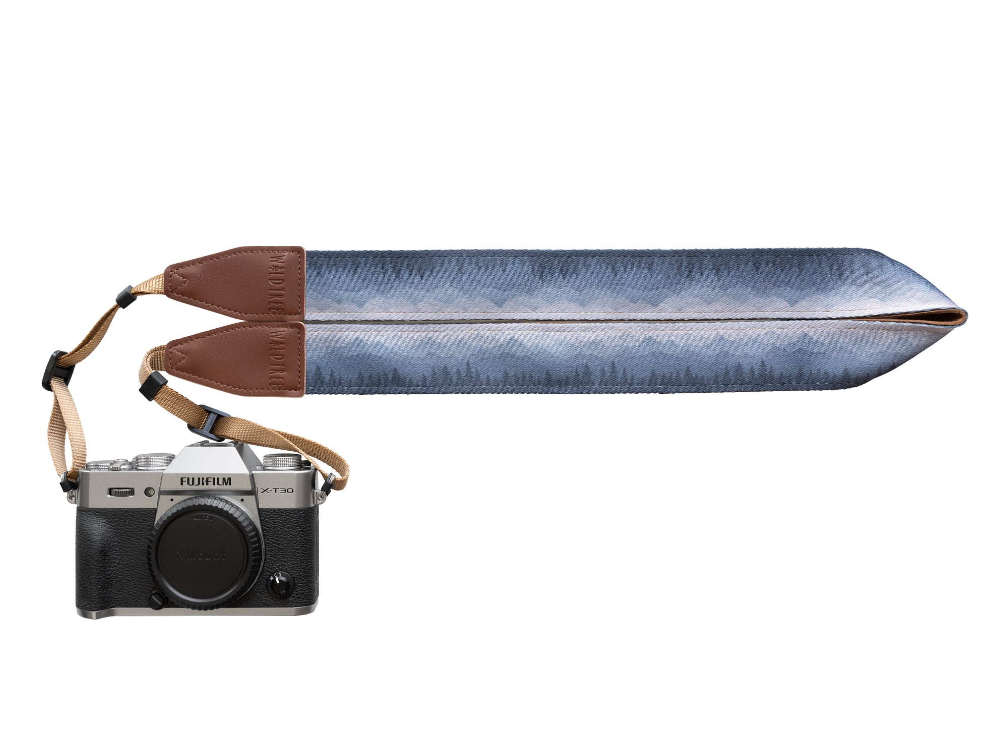 Silent Summit camera strap studio product design shot showing the folded fabric band with a blue-to-gray pine forest gradient illustration and stitched brown leather tips attached to a silver mirrorless camera.