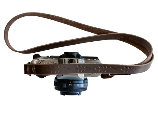 Studio product shot of the vintage slim leather camera strap attached to a silver mirrorless camera, isolated on a clean white background.