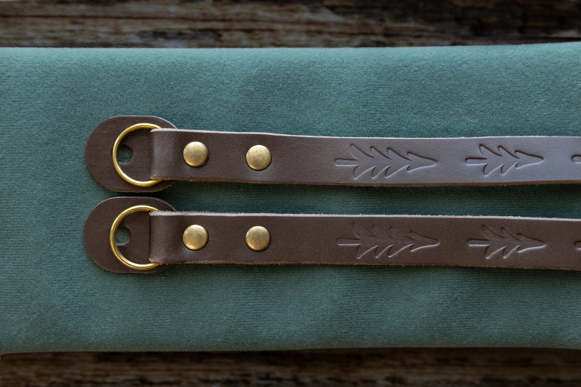Close-up detail of the vintage brown leather camera strap ends, showcasing the hand-stamped tree design, antique bronze rivets, and protective leather O-ring guards.