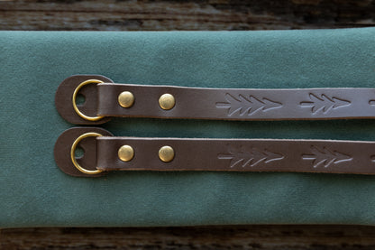 Close-up detail of the vintage brown leather camera strap ends, showcasing the hand-stamped tree design, antique bronze rivets, and protective leather O-ring guards.
