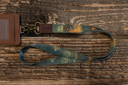 The Smokey Bear lanyard attached to a brown faux-leather ID badge holder (not included) on a rustic wood surface, showing its functionality for work or school.