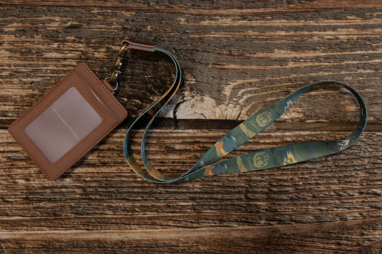 Wide shot of the lanyard and a brown ID card sleeve on a wooden tabletop, emphasizing the vintage aesthetic and the durable antique brass hardware.
