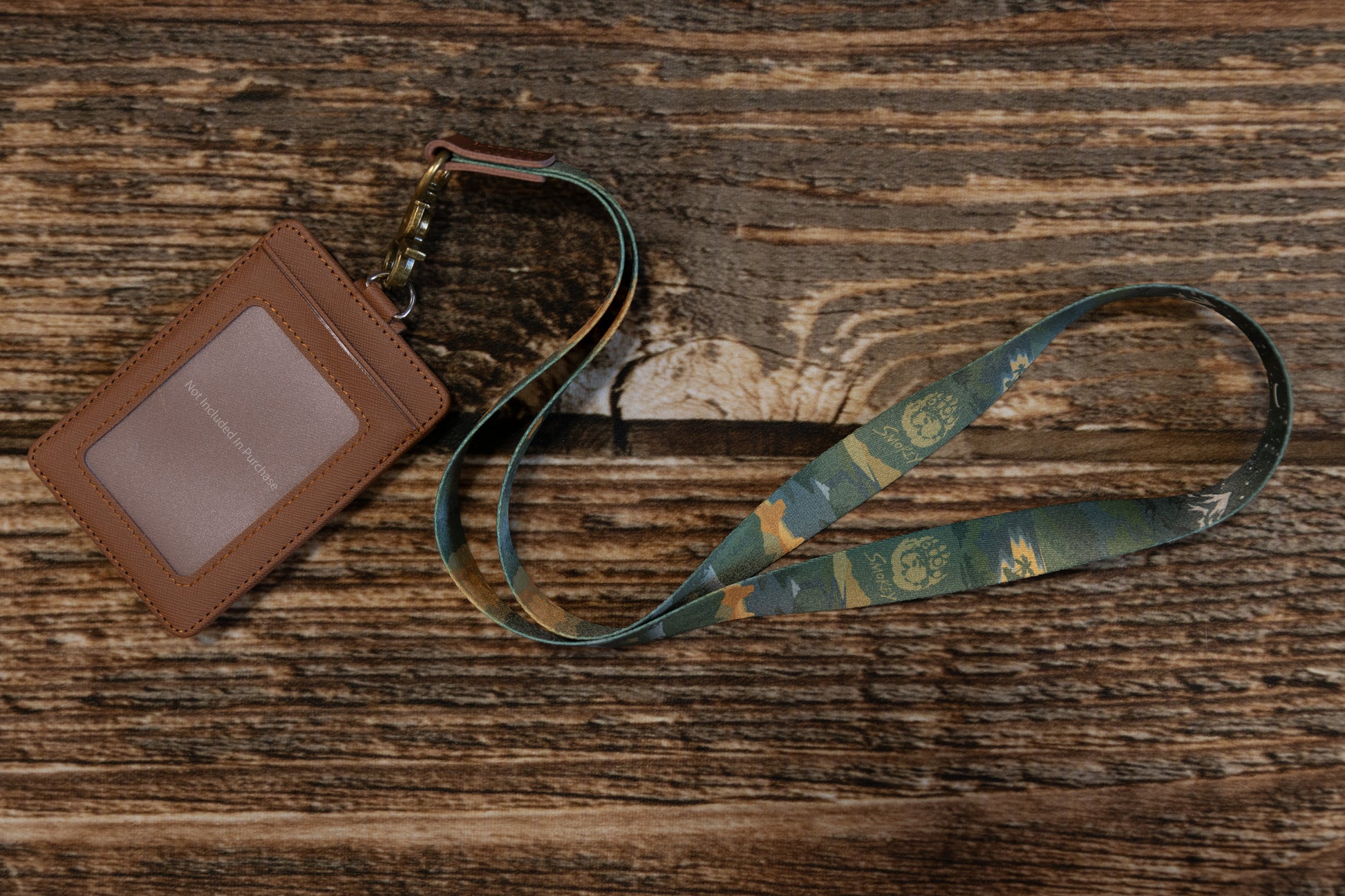 Wide shot of the lanyard and a brown ID card sleeve on a wooden tabletop, emphasizing the vintage aesthetic and the durable antique brass hardware.