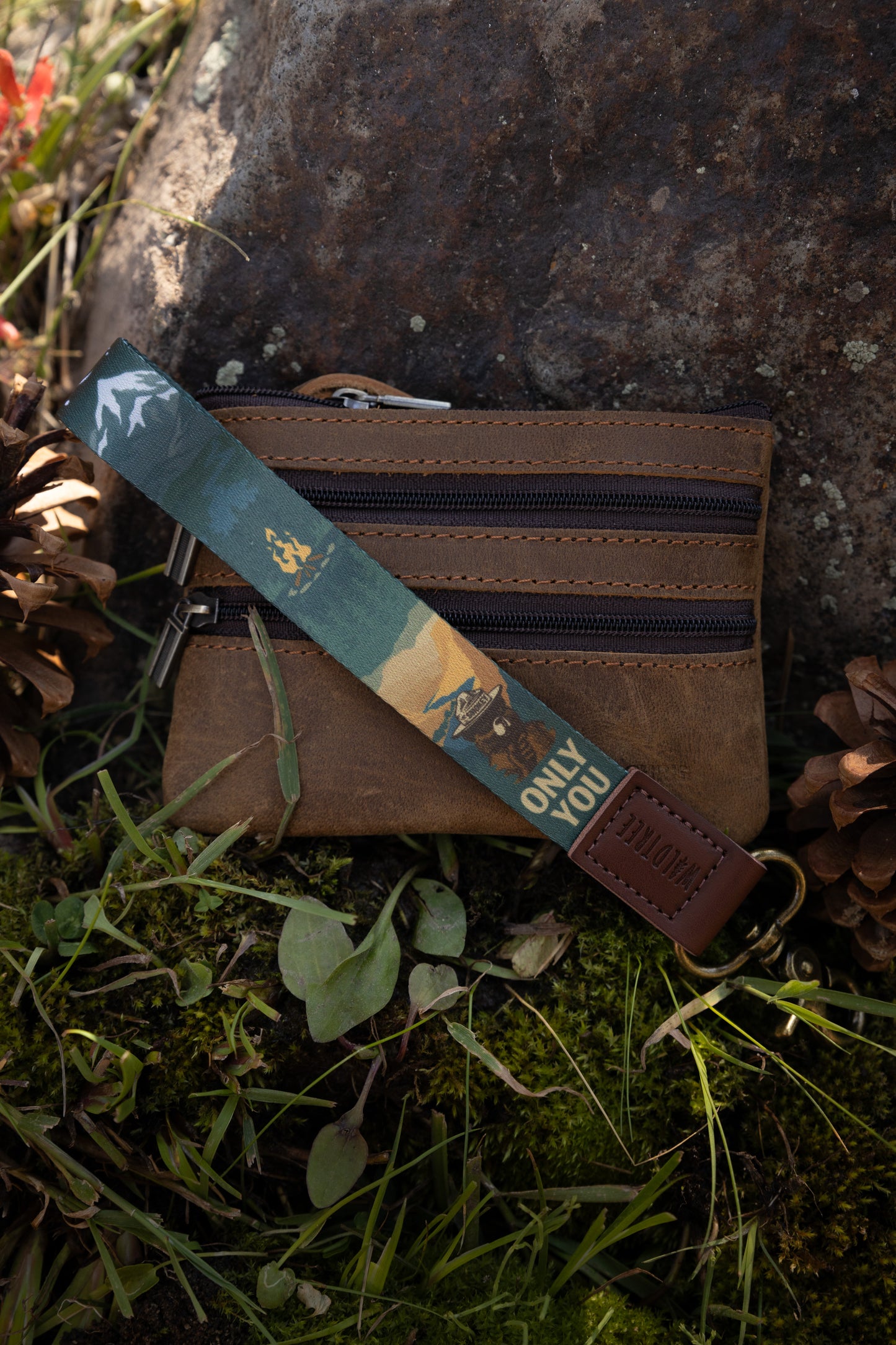 Smokey bear wristlet keychain attached to wallet laying on forest floor