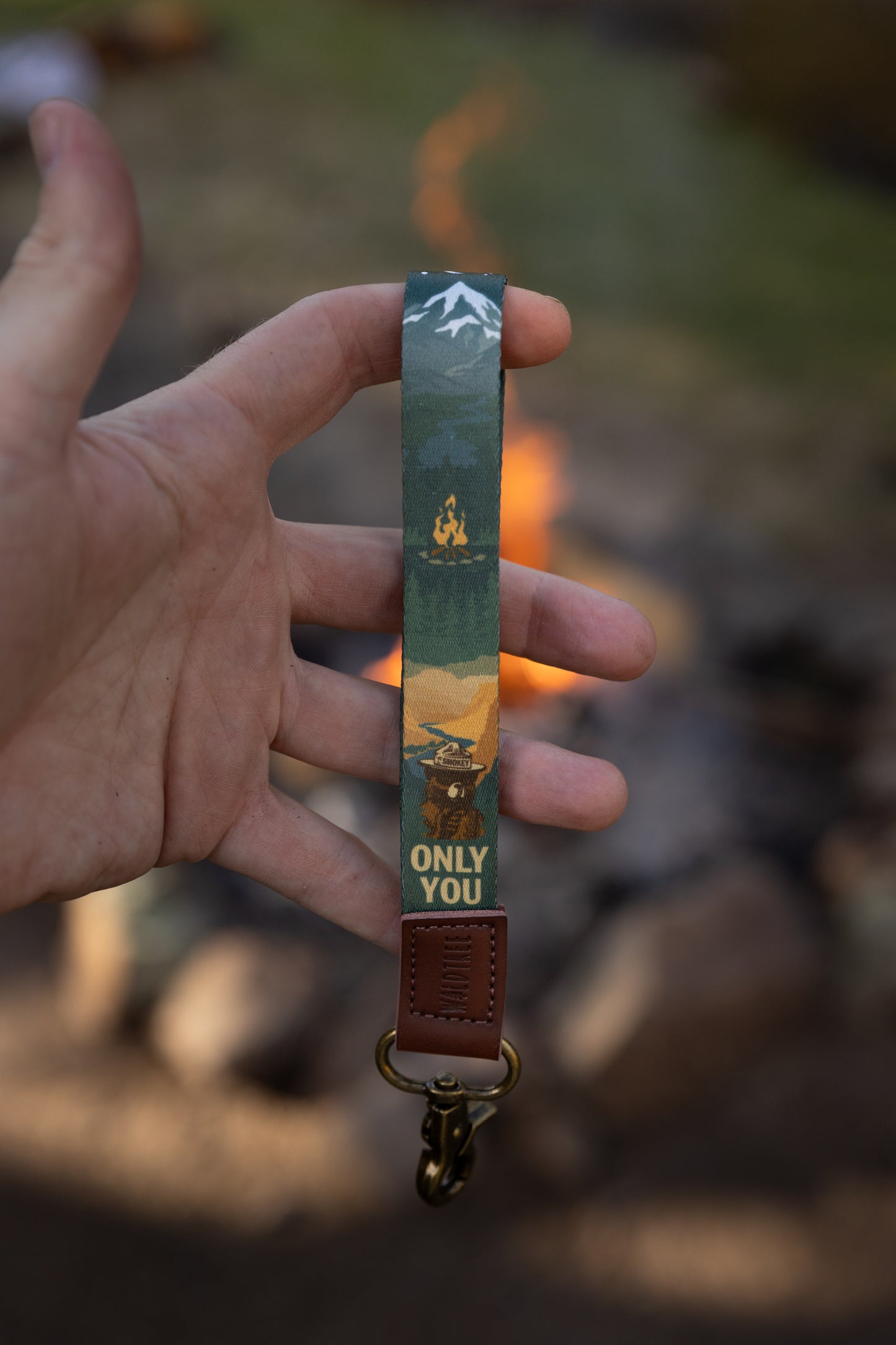 Hand holding out smokey bear wristlet keychain in front of campfire