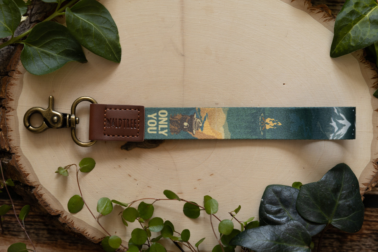 Smokey bear wristlet keychain lying on wood surrounded by plants