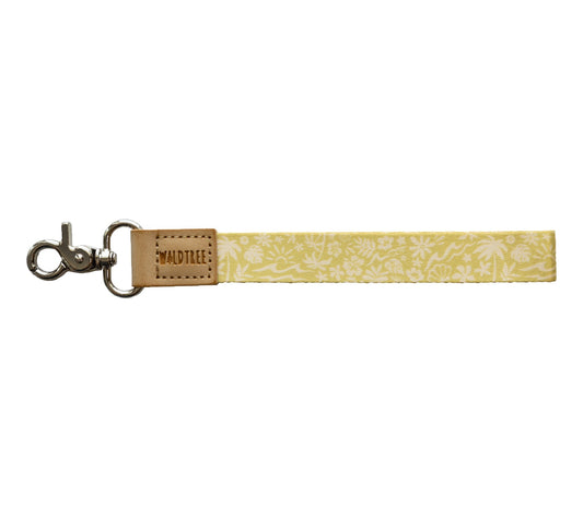 Flat lay of the Sunny Day wristlet keychain on a white background, showing the yellow strap printed with a white beach-themed pattern of waves, palm trees, suns, flowers, and seashells.