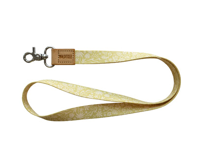 Flat lay of the Sunny Day neck lanyard on a white background, showing the full yellow strap printed with a white beach-themed pattern of waves, palm trees, suns, flowers, and seashells, a tan vegan-leather tab embossed with the WILDTREE logo, and a silver swivel clasp.