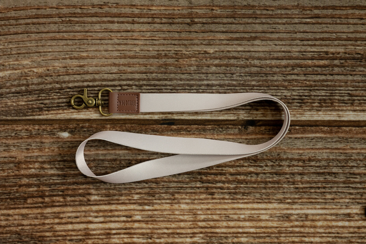 Tan Neck Lanyard coiled on a rustic wood surface, showing the full strap length