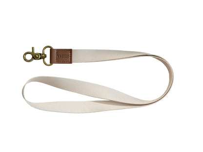 Tan Neck Lanyard laid flat on a white background, showing the cream strap, brown vegan leather patch, and bronze swivel hook