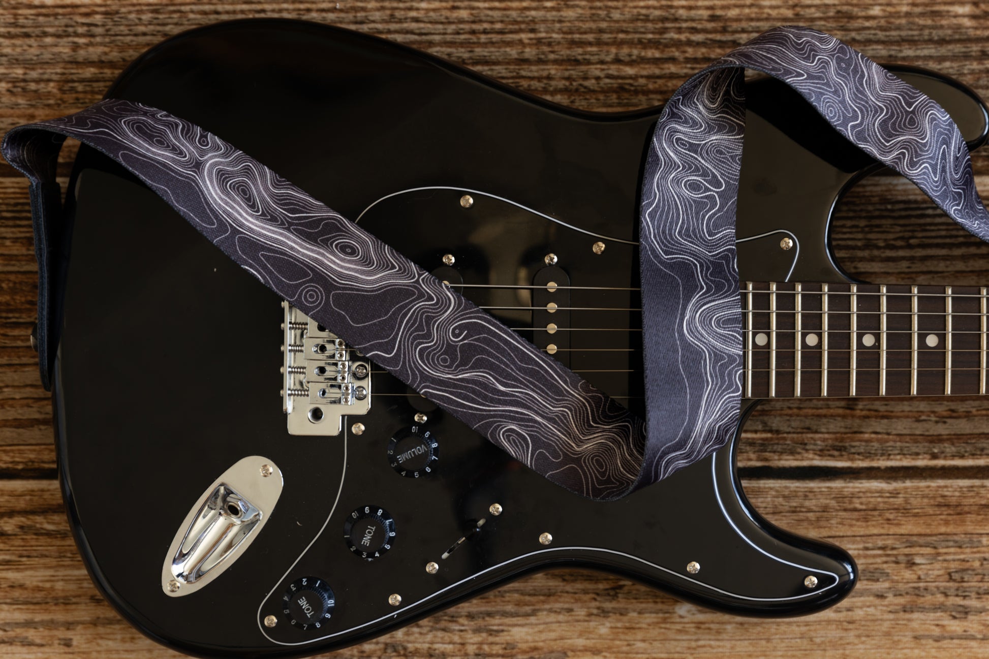 Topographic map designed black and white guitar strap connected to black electric guitar