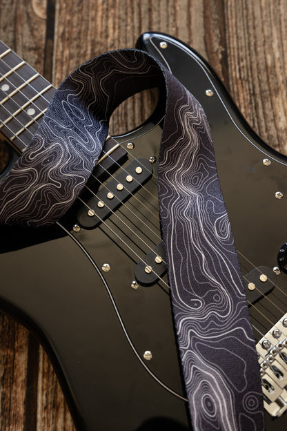 Topographic map designed black and white guitar strap connected to black electric guitar