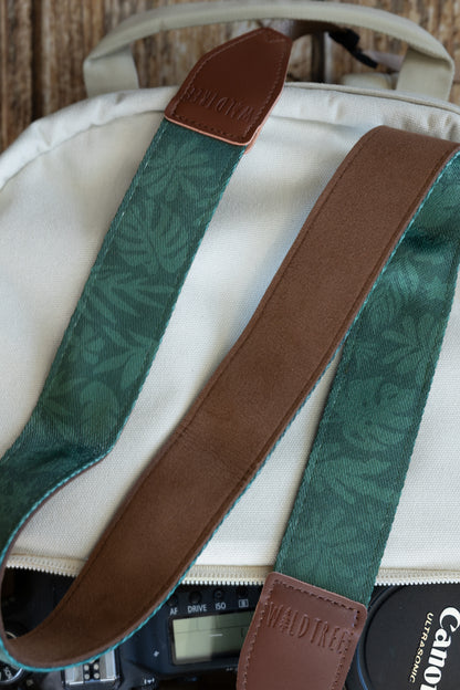Close-up detail shot of the WILDTREE camera strap, showcasing the green tropical leaf printed fabric and the soft, brown faux suede backing.