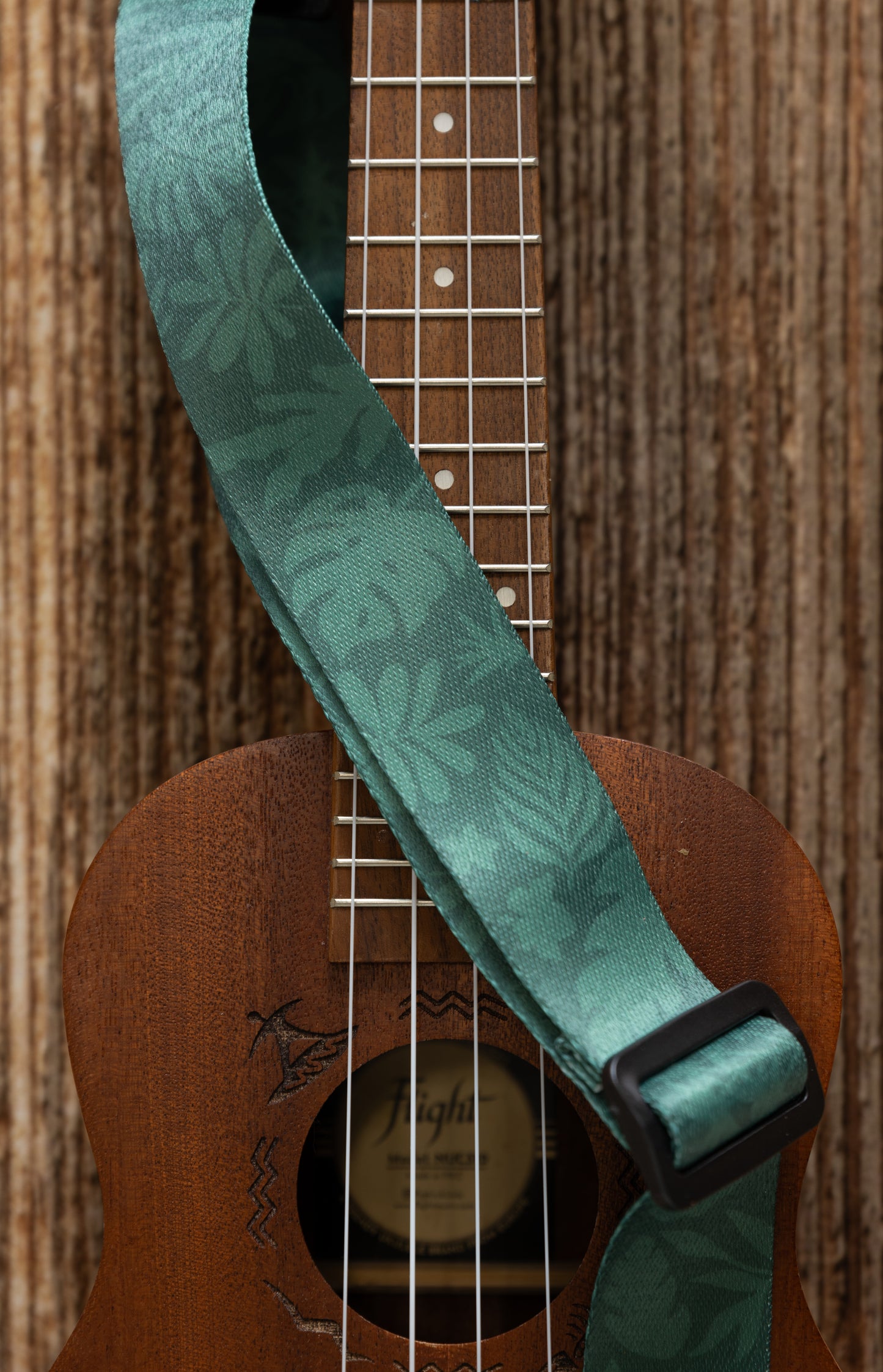 Green tropical leaf printed Ukulele Strap attached to Ukulele lying on wood floor