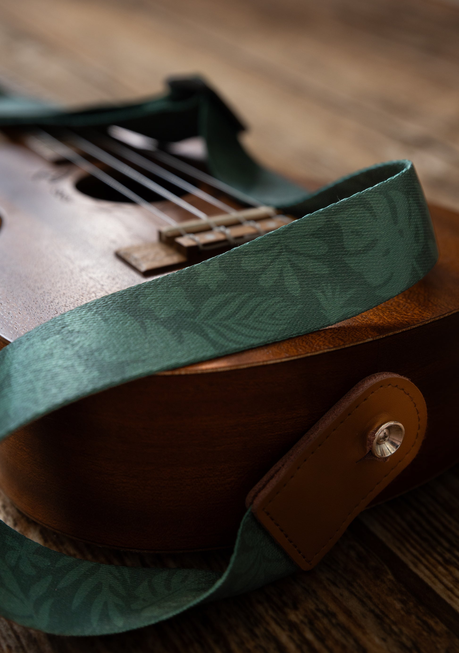 close up Green tropical leaf printed Ukulele Strap attached to Ukulele lying on wood floor