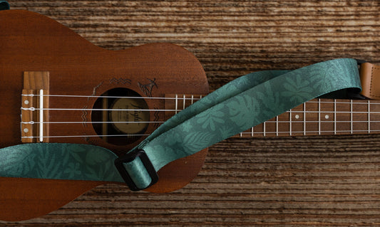 Green tropical leaf printed Ukulele Strap attached to Ukulele lying on wood floor