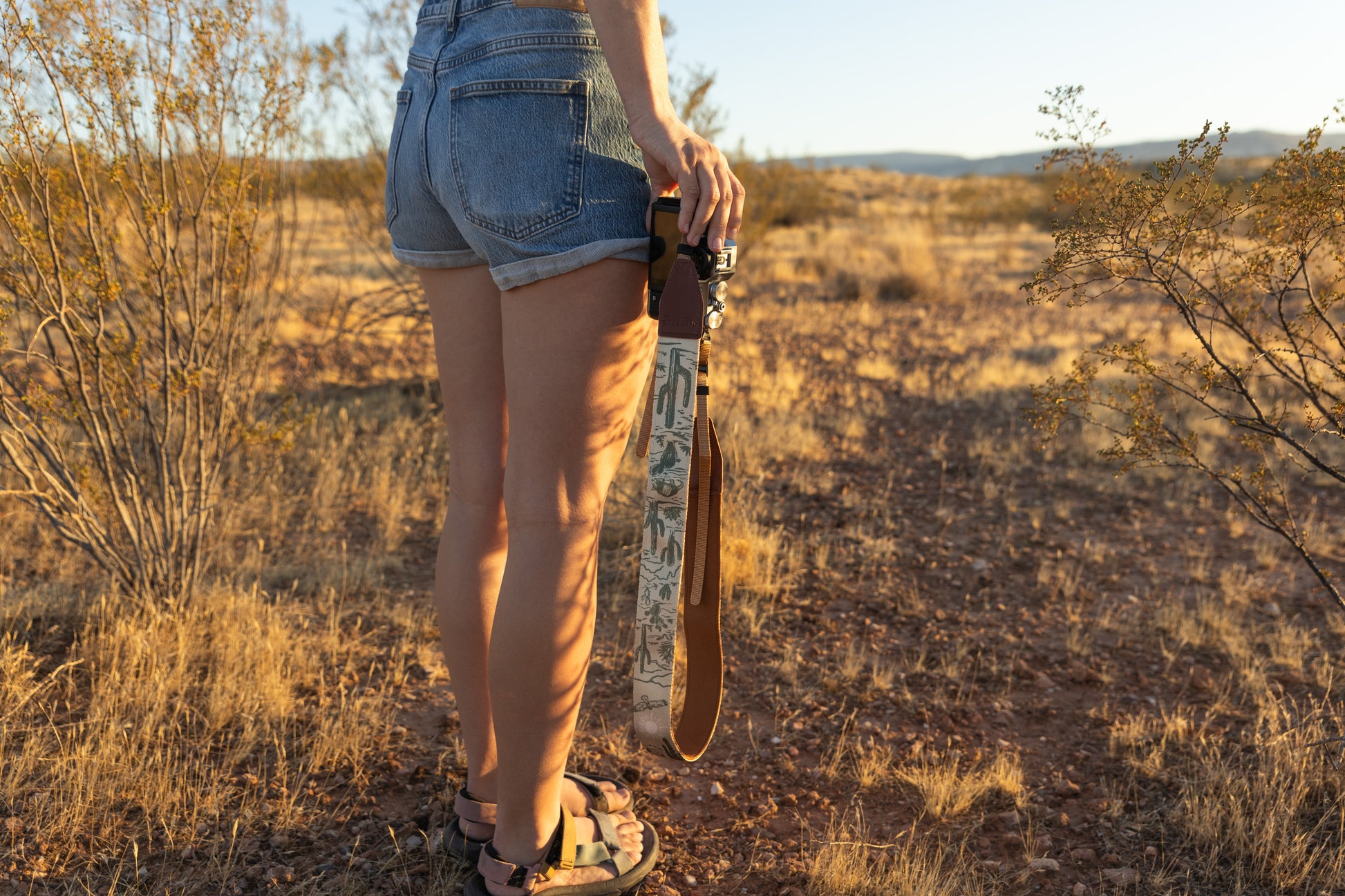 Western landscape camera strap hanging from camera to the side of womens leg