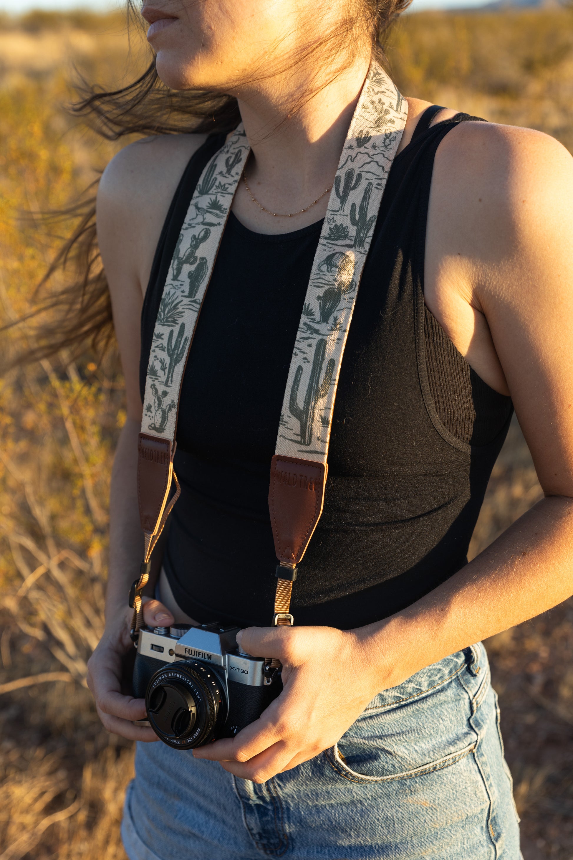 Western landscape camera strap hanging from camera to the side of womens leg