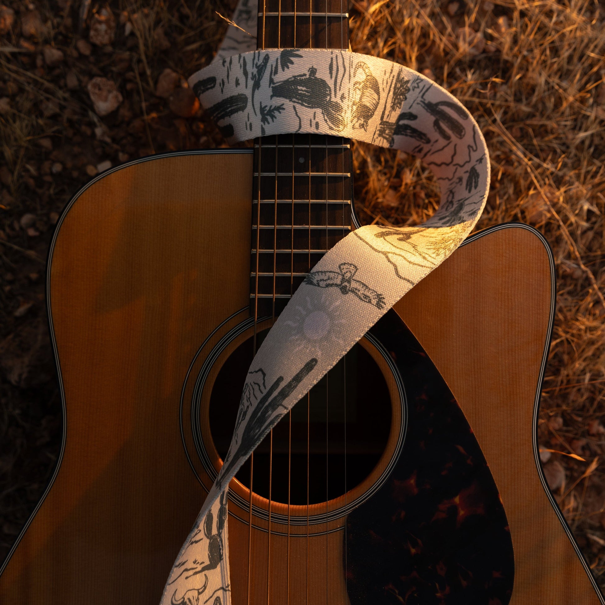 Western landscape guitar strap. Tan strap printed with green desert mountains, wildlife, cacti, bones, birds, snakes, plants