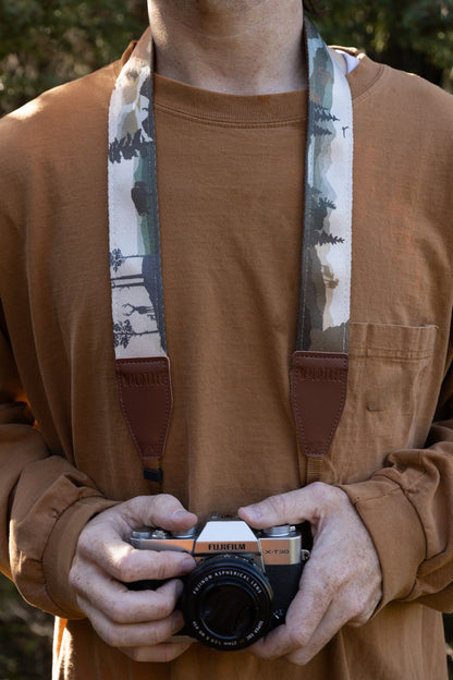 A person wearing the patterned camera strap around their neck, displaying the full breadth of the nature-themed illustration with its muted, earthy color palette and "WILDTREE" leather accents.