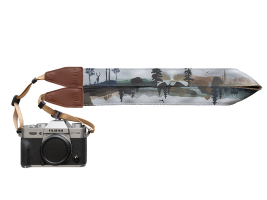 A studio-style shot of a camera attached to the strap, fully extended to reveal the complete, panoramic nature design printed along the length of the strap fabric with "WILDTREE" branding visible on the leather end.