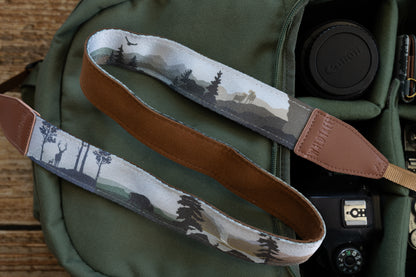 A top-down view of the camera strap, showing both the printed outer fabric featuring wildlife silhouettes and the soft, brown suede-like inner lining, with leather ends branded "WILDTREE".