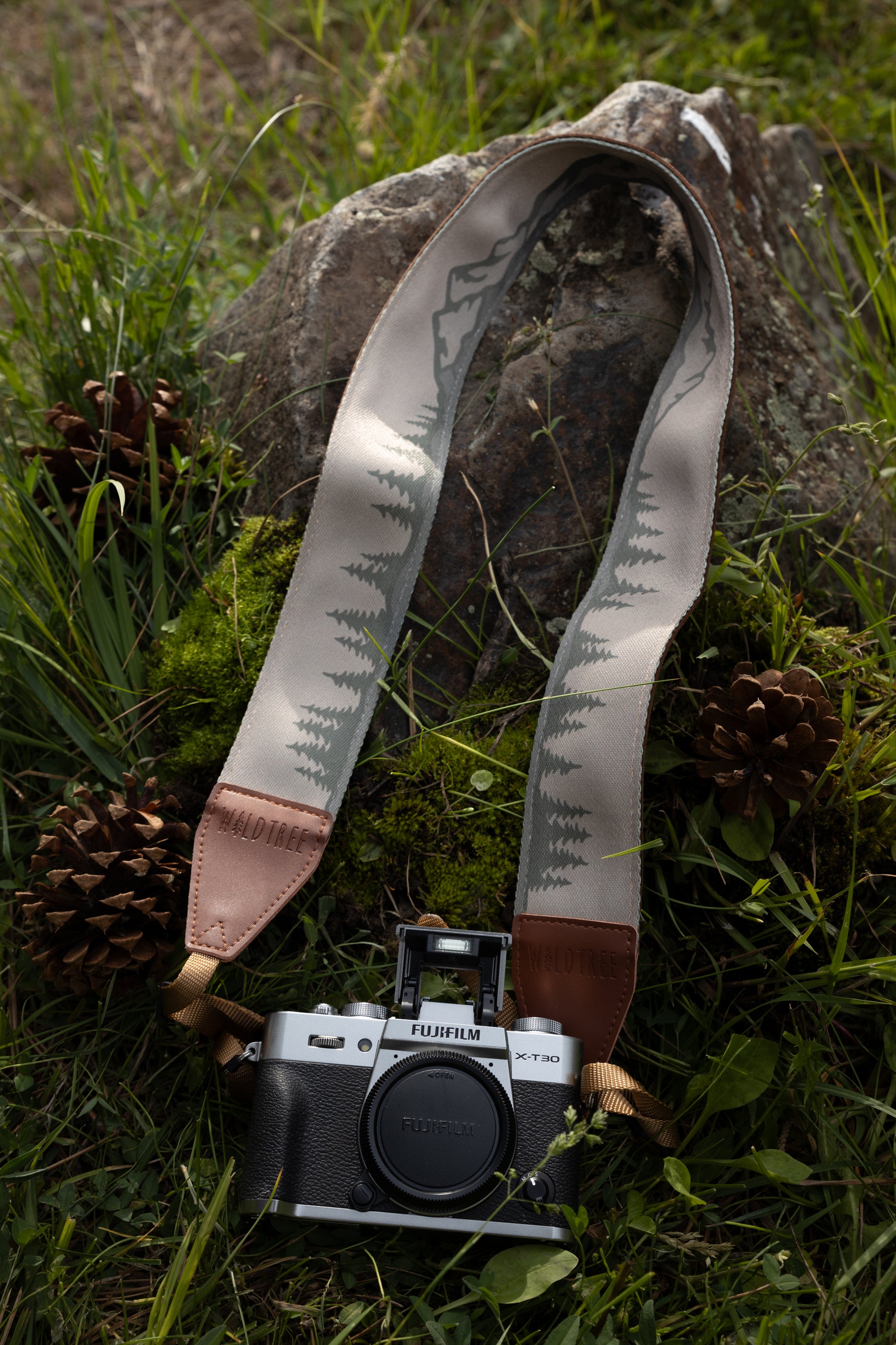 Wildtree camera strap printed with trees and mountains laying on forest floor connected to fujifilm x-t30 camera