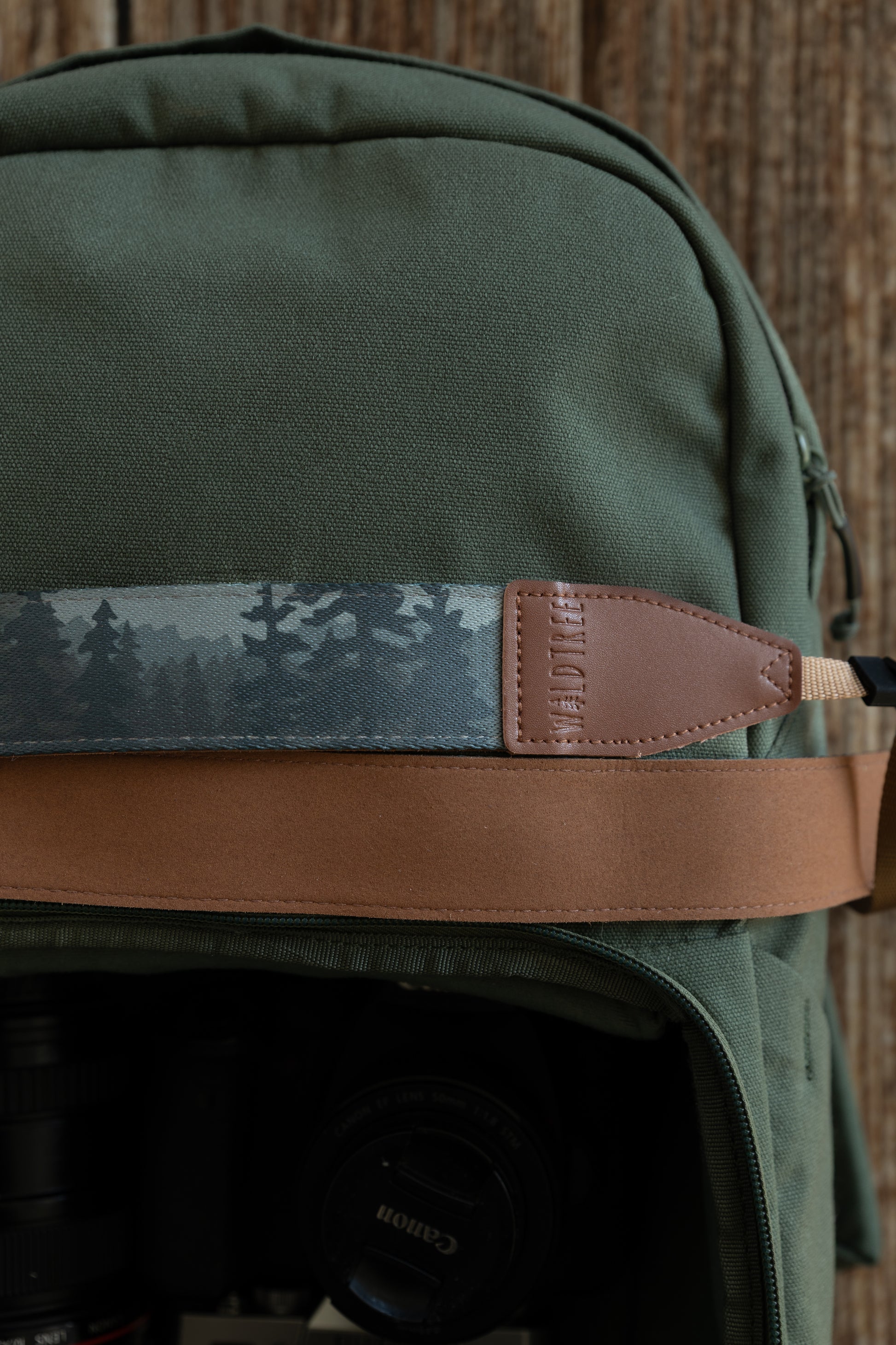 A horizontal close-up of the strap resting on a green bag, clearly showing the silhouette of evergreen trees in the misty landscape print and the stitched vegan leather end piece.