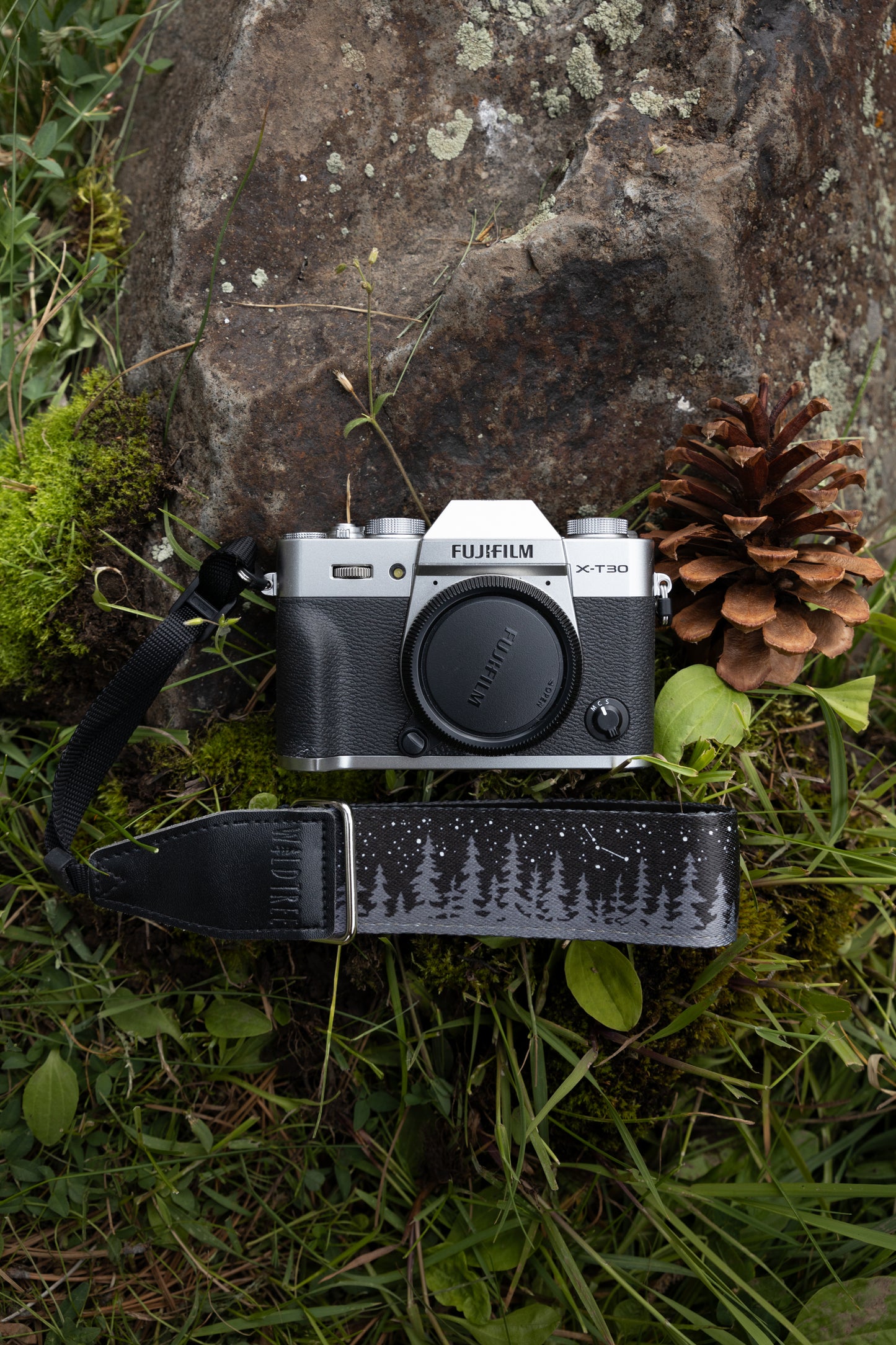 black camera wrist strap printed with trees and stars laying on forest floor