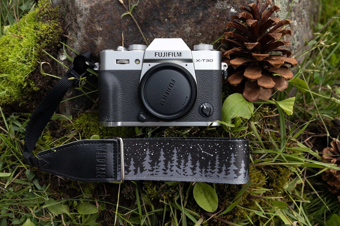 black camera wrist strap printed with trees and stars laying on forest floor