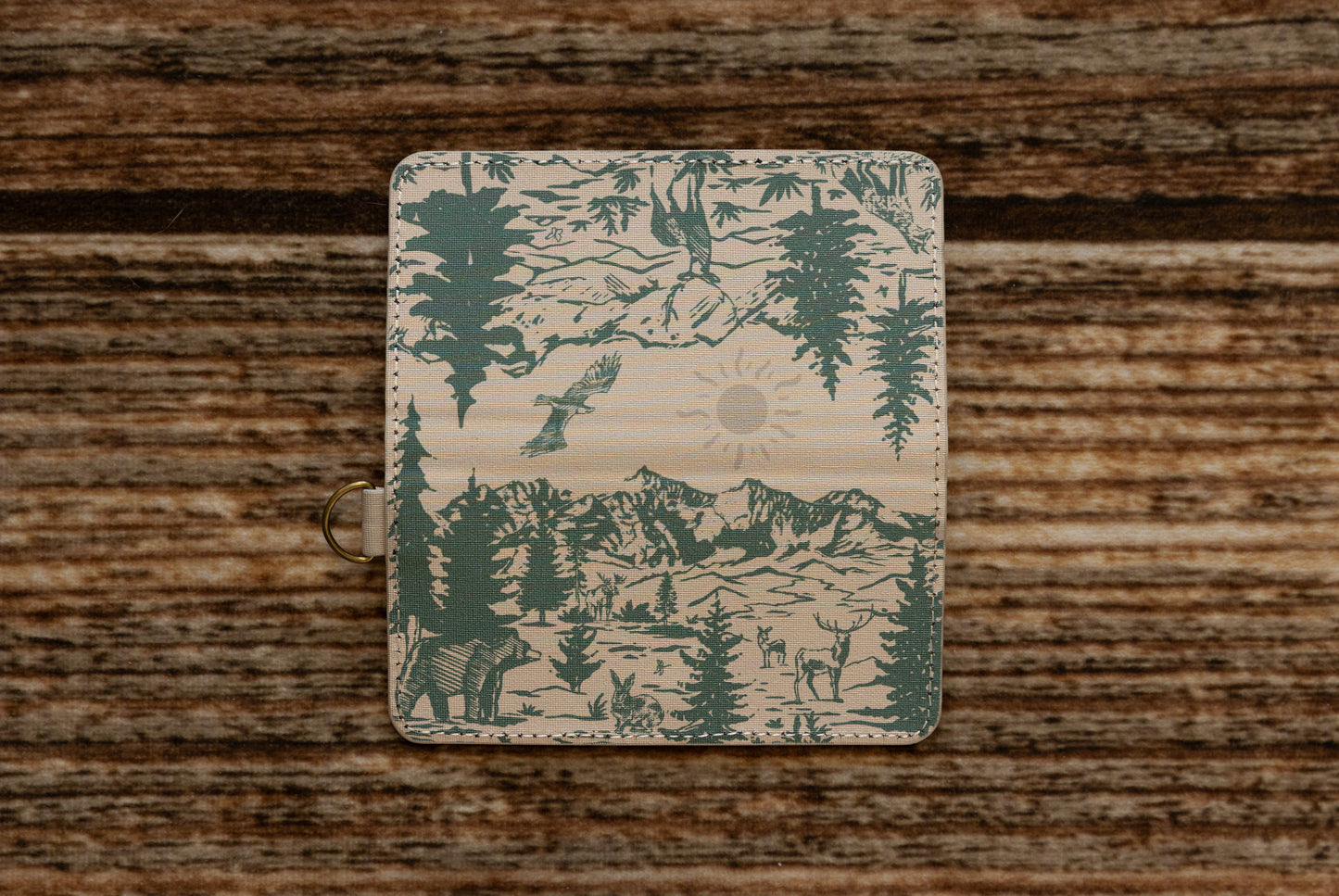 A flat layout of the full wrap-around illustration on the WILDTREE SD card caddy, showcasing an eagle, mountains, evergreen trees, a bear, a rabbit, and a deer in forest green ink.