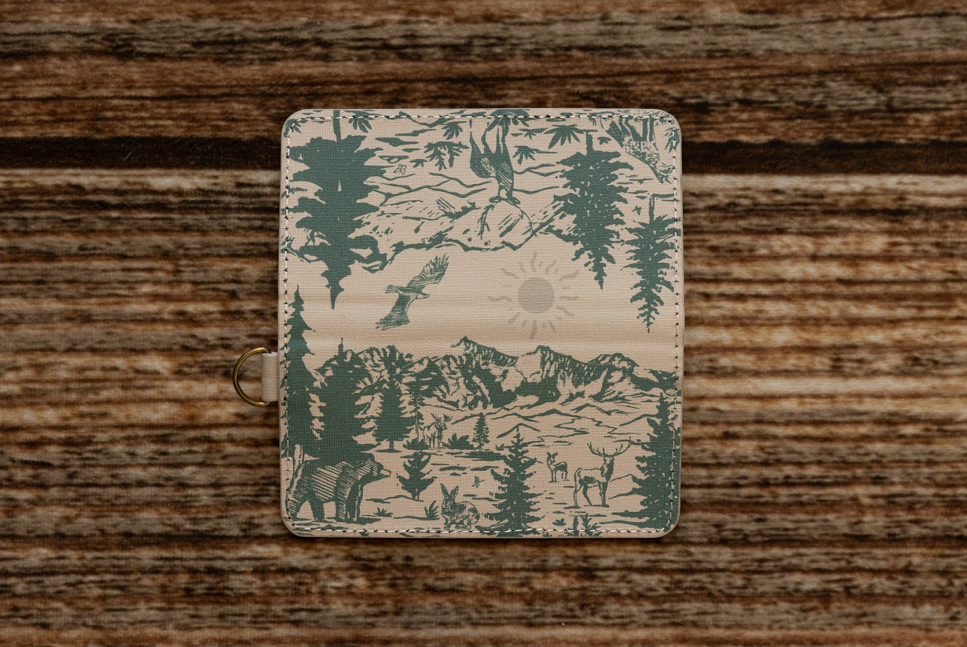 A flat layout of the full wrap-around illustration on the WILDTREE SD card caddy, showcasing an eagle, mountains, evergreen trees, a bear, a rabbit, and a deer in forest green ink.