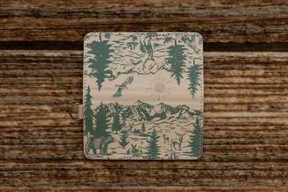 A flat layout of the full wrap-around illustration on the WILDTREE SD card caddy, showcasing an eagle, mountains, evergreen trees, a bear, a rabbit, and a deer in forest green ink.