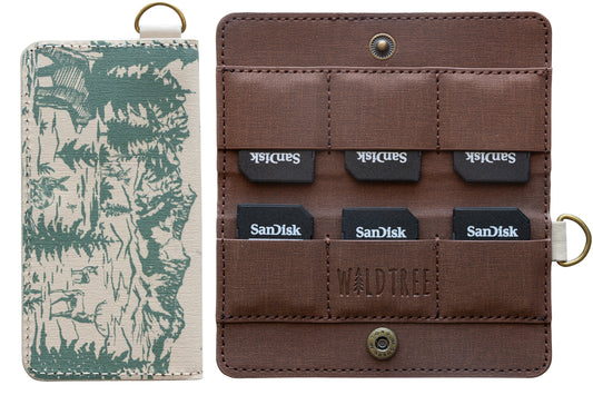 A product photo on a white background showing the interior and exterior of the WILDTREE SD card holder. The left side shows the closed case with a green forest and mountain illustration on tan fabric. The right side shows the open brown interior with six SanDisk SD cards tucked into individual slots and a debossed WILDTREE logo.