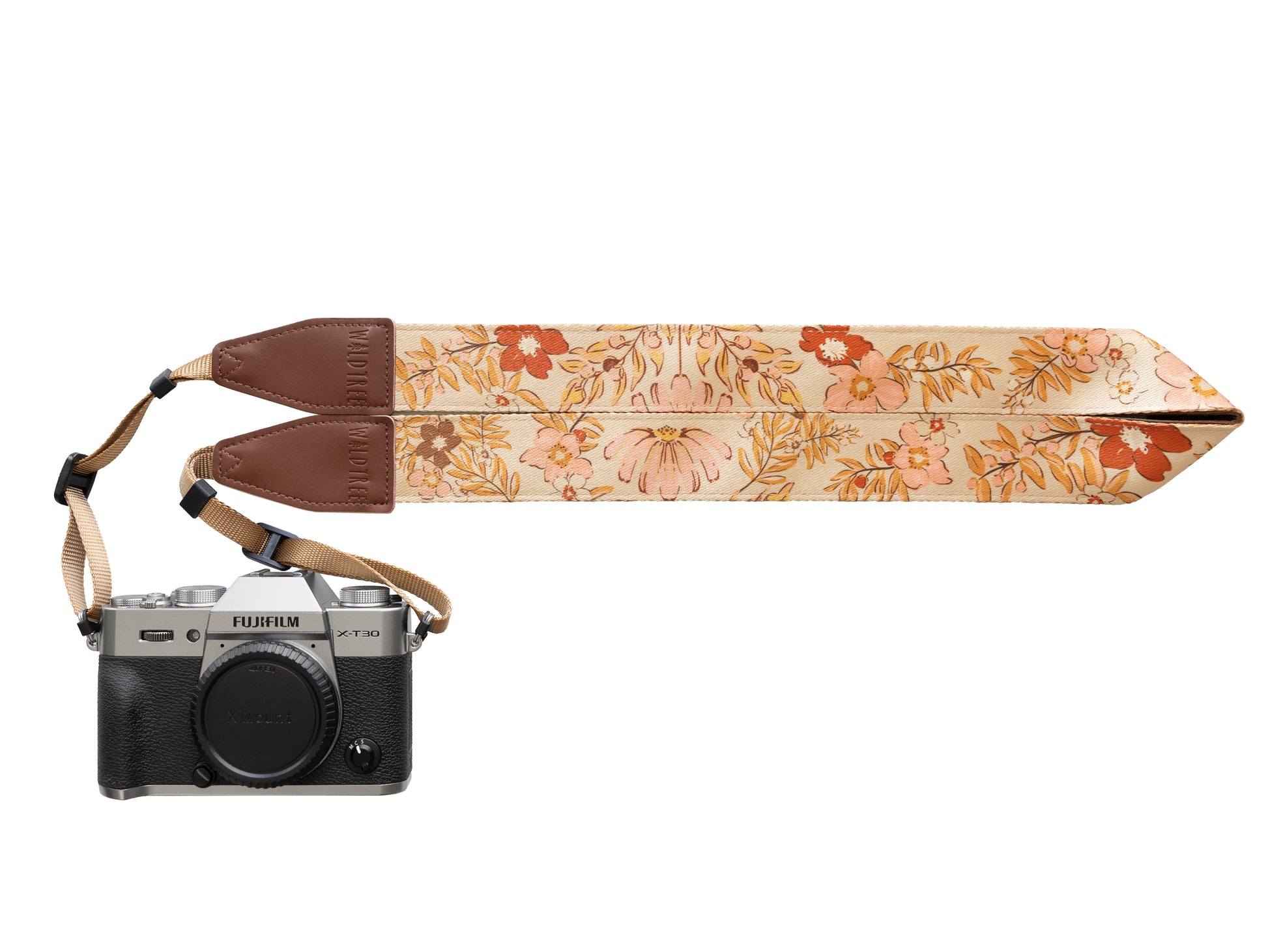 A product studio shot against a white background featuring a silver Fujifilm X-T30 camera attached to a wide "Mellow Meadow" floral strap. The strap is laid out horizontally to showcase the full repeat of the vintage botanical pattern and the brown leather brand accents.