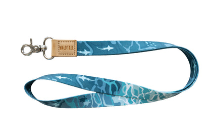 A blue and teal lanyard with an ocean-themed pattern of sharks and sea turtles is shown against a white background. It has a tan leather tab with "WILDTREE" embossed on it.