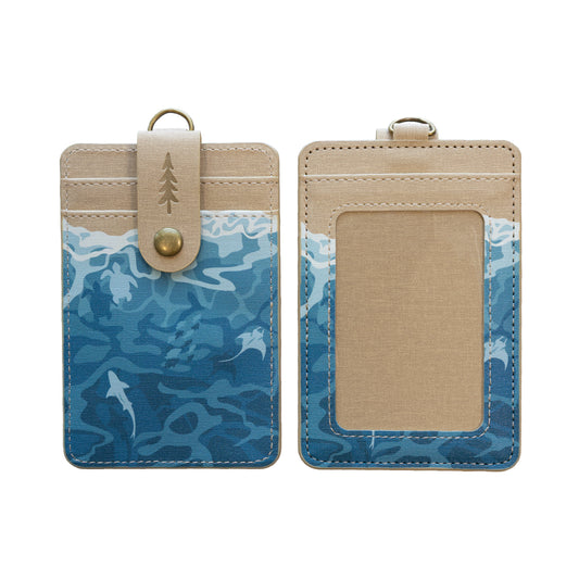 Front and back of the Ocean ID badge holder, featuring a blue wave pattern with shark and stingray silhouettes, a tan top panel with an embossed pine tree logo, and a clear card window on the back.