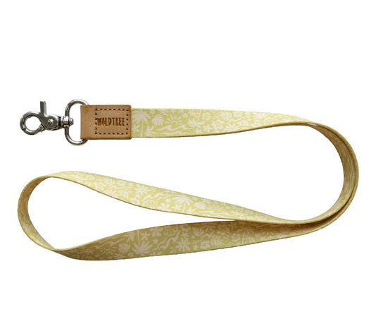 Flat lay of the Sunny Day neck lanyard on a white background, showing the full yellow strap printed with a white beach-themed pattern of waves, palm trees, suns, flowers, and seashells, a tan vegan-leather tab embossed with the WILDTREE logo, and a silver swivel clasp.