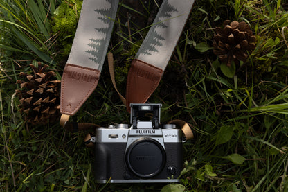 Wildtree camera strap printed with trees and mountains laying on forest floor connected to fujifilm x-t30 camera