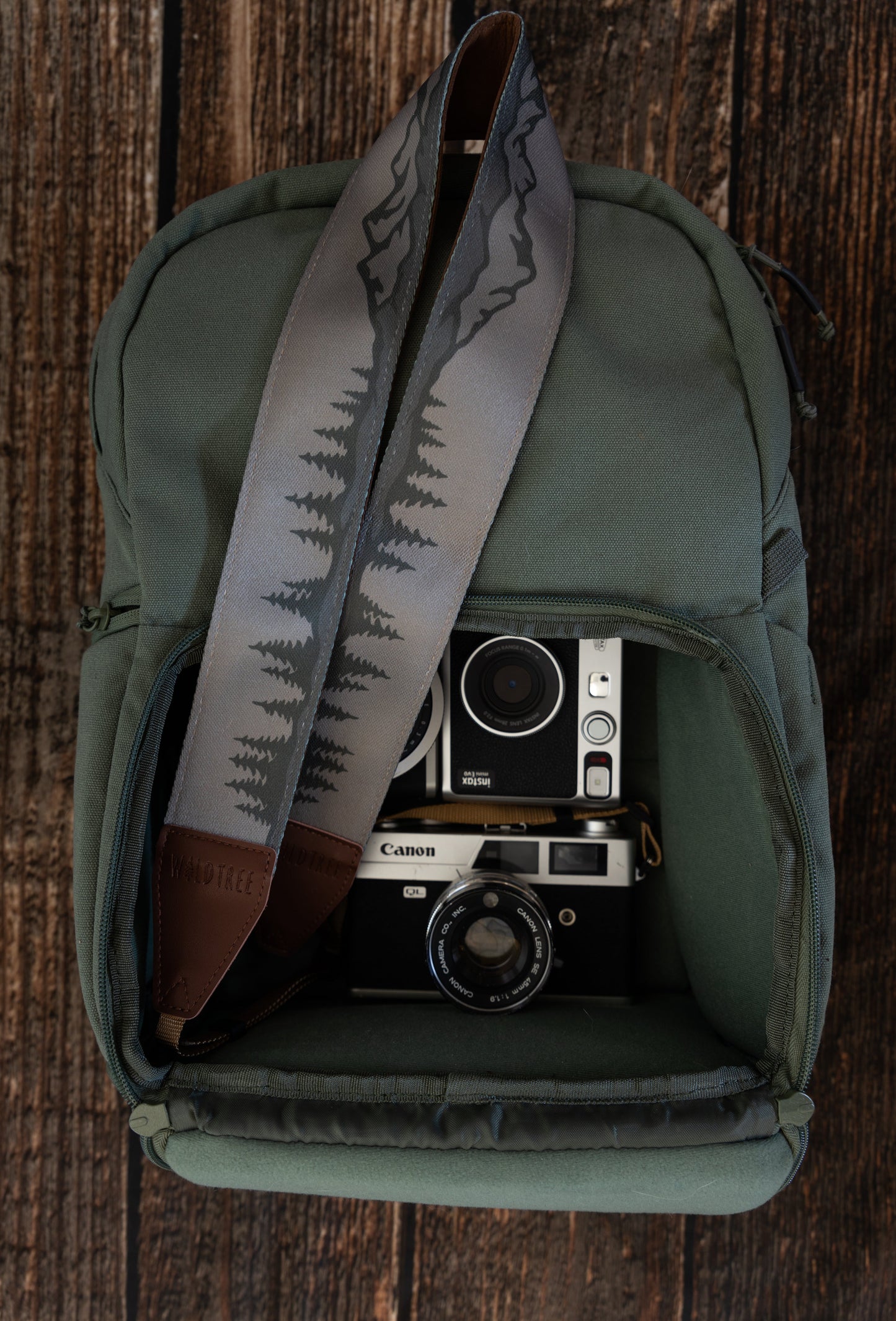 Wildtree camera strap printed with trees and mountains laying on green backpack with camera gear