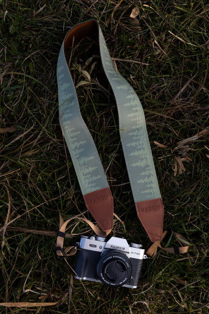 Green camera strap printed with green pine trees across the length of the strap. Connected to camera