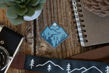 Load image into Gallery viewer, Blue Mountain Sticker wood background surrounded by notebook, camera and succulent
