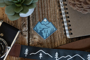 Blue Mountain Sticker wood background surrounded by notebook, camera and succulent