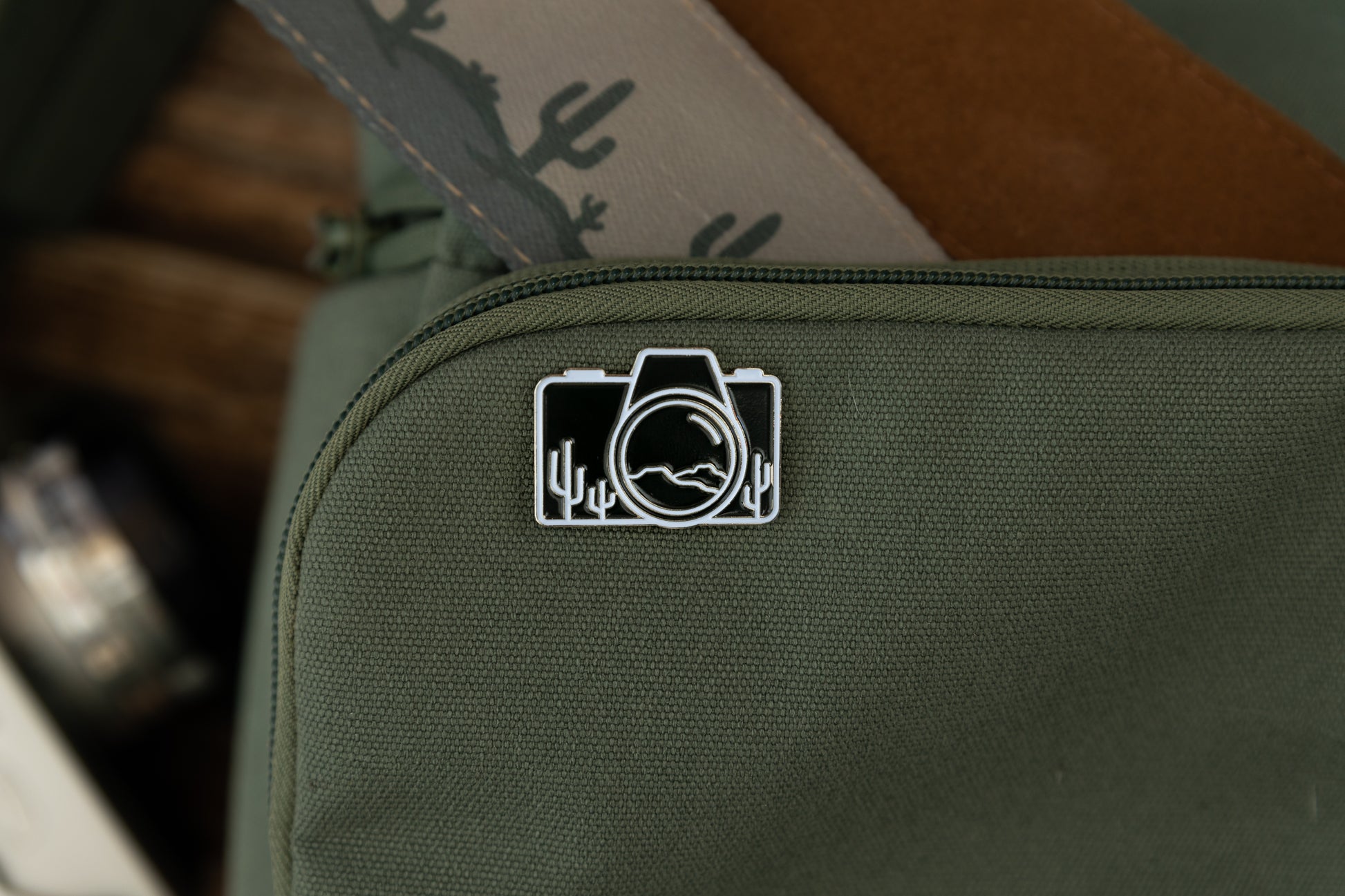 Camera shaped enamel pin with desert mountains and cacti 