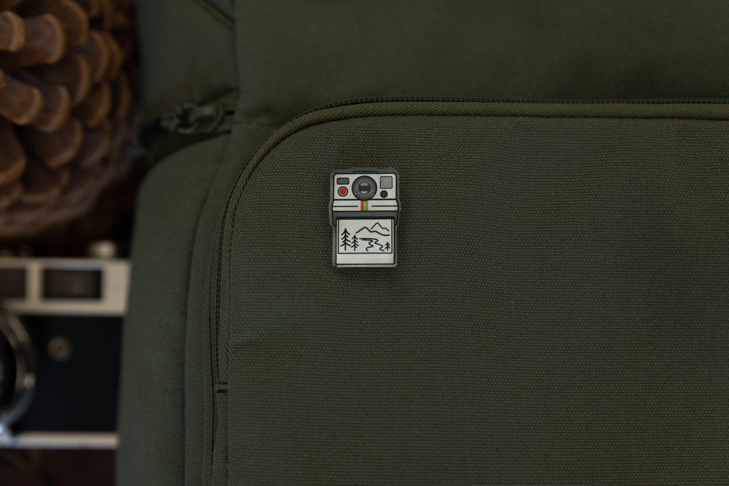acrylic pin of a polaroid camera pinned to backpack